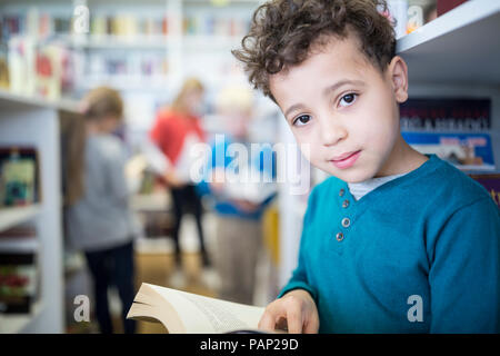 Portrait of smiling schoolboy with book in school library Stock Photo