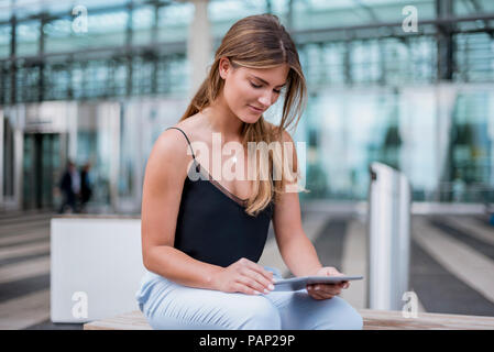 Smiling young woman sitting outdoors using tablet Stock Photo