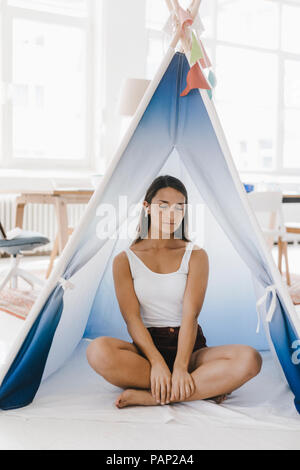 Young woman sitting cross-legged in a tent at home, with eyes closed Stock Photo