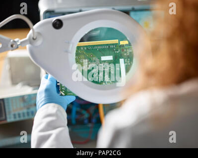 Female technician checking circuit board with magnifier Stock Photo