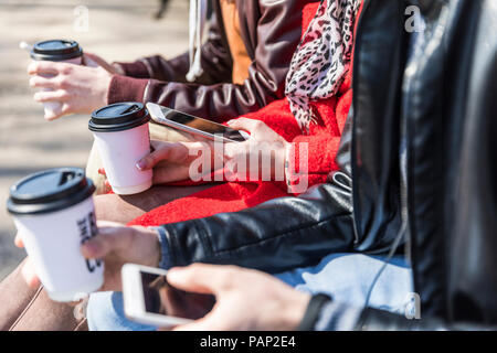Russia, Moscow, details of three friends holding smartphones and coffee to go Stock Photo
