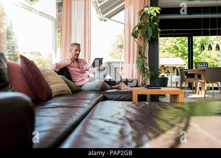 Mature man sitting on couch at home using a tablet Stock Photo