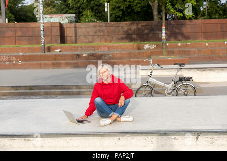 Senior woman wearing red hoodie using laptop outdoors Stock Photo