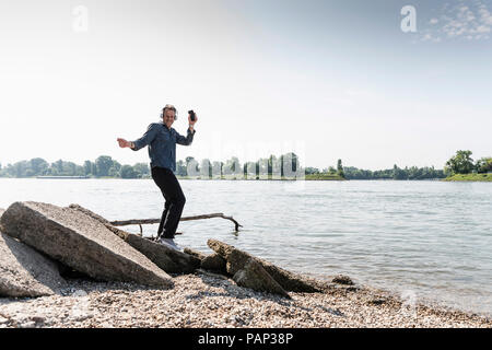 Mature man with smartphone dancing at Rhine riverbank Stock Photo
