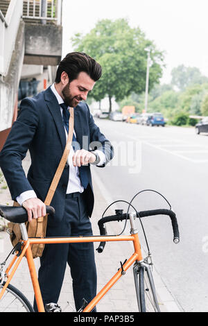 Smiling businessman with bicycle at the street checking the time Stock Photo