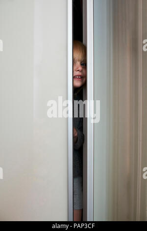 Smiling little girl hiding in wardrobe Stock Photo