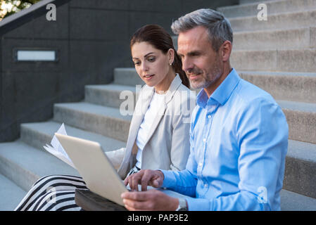 Two business people sitting side by side on stairs working together Stock Photo