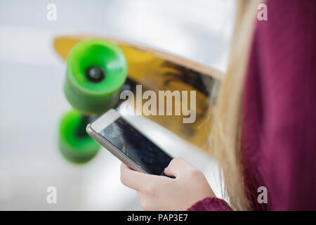 Close-up of teenage girl holding skateboard and cell phone Stock Photo