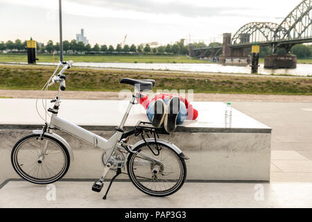 Senior woman with city bike having a break lying on platform Stock Photo