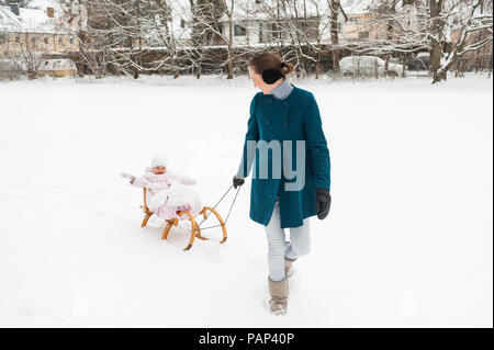 Mother pulling little daughter on sledge Stock Photo