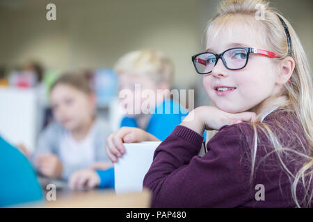 Portrait of smiling schoolgirl with classmates in class Stock Photo