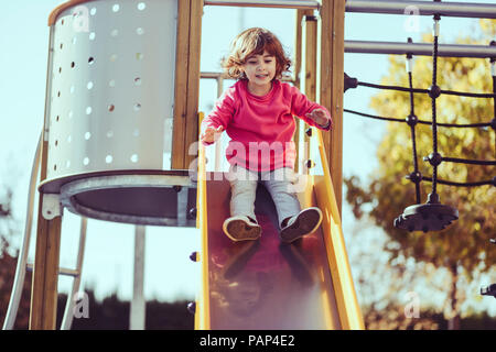 Portrait of little girl sitting on slide at playground Stock Photo
