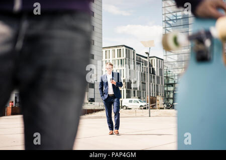 Mature businessman using cell phone and man with longboard in foreground Stock Photo