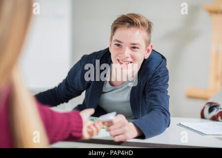 Smiling teenage boy passing a note to a girl in class Stock Photo