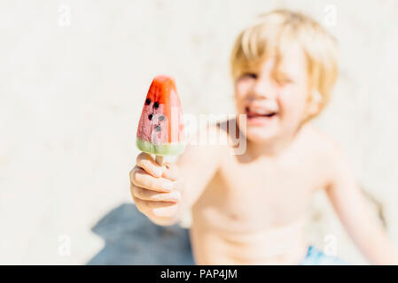 Happy boy holding a watermelon ice lolly on the beach Stock Photo