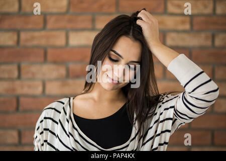 Portrait of smiling young woman in front of brick wall Stock Photo