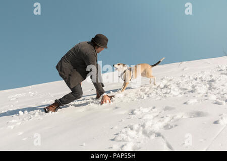 Man playing with dog in winter, throwing snow Stock Photo