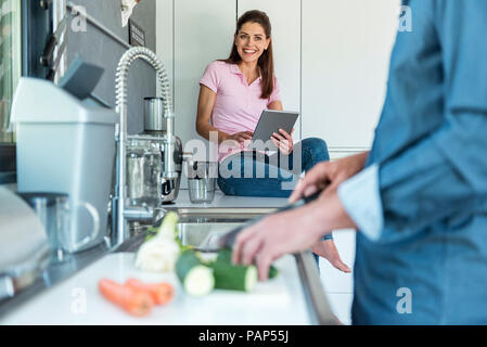 Happy couple in kitchen at home cooking and using a tablet