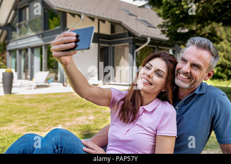 Happy couple sitting in garden of their home taking a selfie Stock Photo