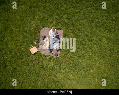 Bird's eye view of woman sitting on blanket on meadow with dog using tablet Stock Photo