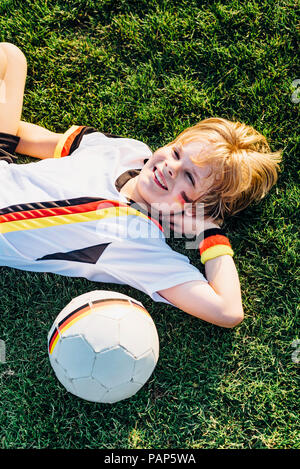 Boy in German soccer shirt lying on grass, smiling Stock Photo