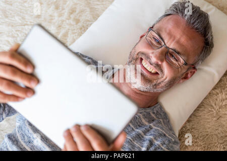 Mature man lying on pillow using a tablet Stock Photo