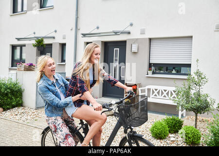 Two happy young women riding bicycle together on one bike Stock Photo