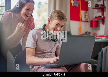 Happy teenage girl watching boy using laptop Stock Photo
