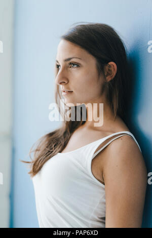 Young woman leaning against wall, looking at distance Stock Photo