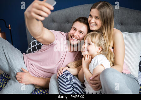 Happy family sitting on bed, taking smartphone selfies Stock Photo