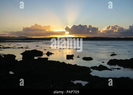 Golden clouds and light from sun rays during rocky island beach sunset in Siargao, Philippines Stock Photo