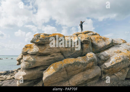 France, Brittany, Meneham, woman standing on rock formation at the coast Stock Photo