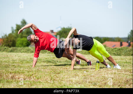 Couple doing side plank exercise on meadow Stock Photo