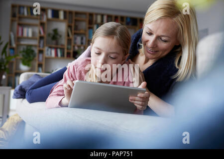 Mother and daughter lying on couch, using digital tablet Stock Photo