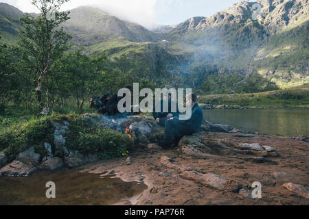 Norway, Lofoten, Moskenesoy, Young men sitting at camp fire at Agvatnet lake Stock Photo