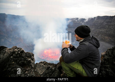 Africa, Democratic Republic of Congo, Virunga National Park, Man sittiing over Nyiragongo volcano crater Stock Photo