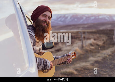 Iceland, young man sitting in van and playing guitar Stock Photo