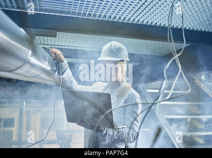 Female technician working on pipeworks, using laptop Stock Photo