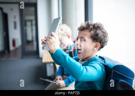 Happy schoolboy holding up tablet on corridor in school Stock Photo