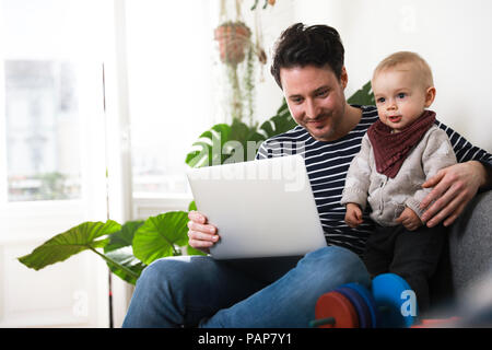 father sitting on couch with his little daughter, using laptop Stock Photo
