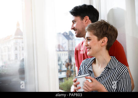 Relaxed couple standing at the window, woman drinking coffee Stock Photo