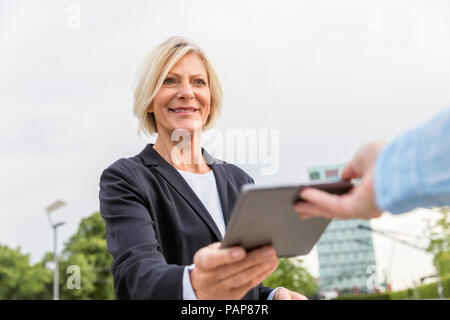 Smiling senior businesswoman handing over tablet outdoors Stock Photo