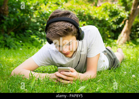 Boy lying on meadow listening music with headphones and smartphone Stock Photo