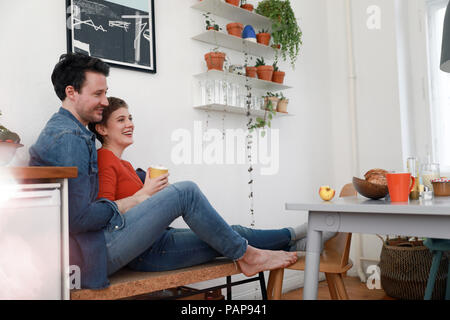 Happy couple sitting in kitchen, leaning against each other Stock Photo