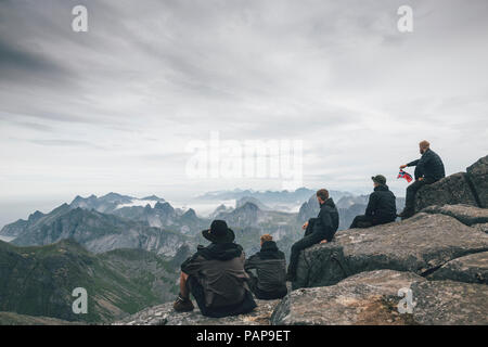 Norway, Lofoten, Moskenesoy, Young men sitting at Hermannsdalstinden, looking over Kjerkefjord Stock Photo