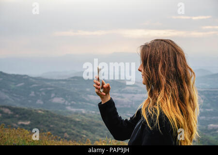Spain, Barcelona, young woman taking selfie with smartphone on Montcau Mountain Stock Photo