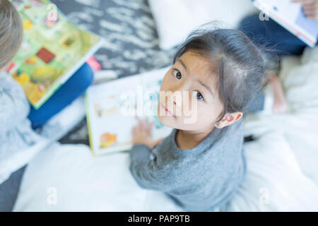 Portrait of schoolgirl sitting on the floor with book in school Stock Photo