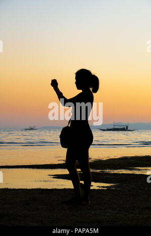 Silhouette profile of a young lady taking pictures during a beach sunset - Alona Beach, Bohol - Philippines Stock Photo