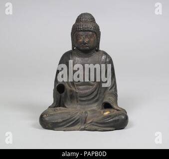 Seated Buddha. Culture: Japan. Dimensions: H. 6 5/8 in. (16.9 cm); W. 5 1/4 in. (13.3 cm); D. 4 1/8 in. (10.5 cm). Date: 10th-11th century.  This small image probably represents Shakyamuni, the historical Buddha, in his enlightened state, seated in the posture of meditation. Short whorls of hair (rahotsu) cover the head, and a cranial protuberance symbolizes his profound wisdom. The hands, which were cast separately, would have formed the characteristic mudras associated with his image: the right, raised and open in a gesture of reassurance, represents the benevolent gift of life without fear  Stock Photo