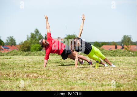 Couple doing side plank exercise on meadow Stock Photo